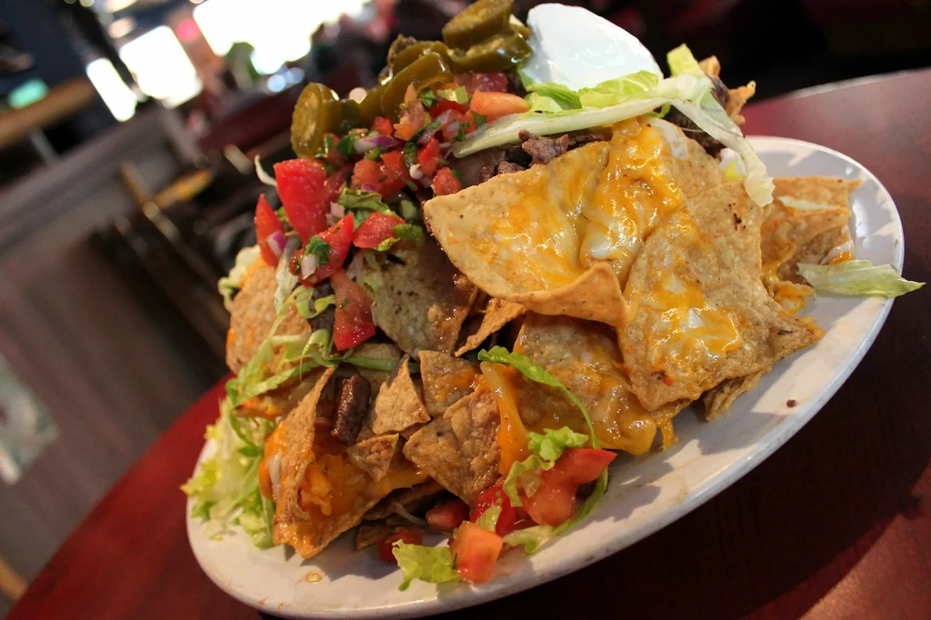 Large plate of beef nachos with melted cheese and assorted toppings.