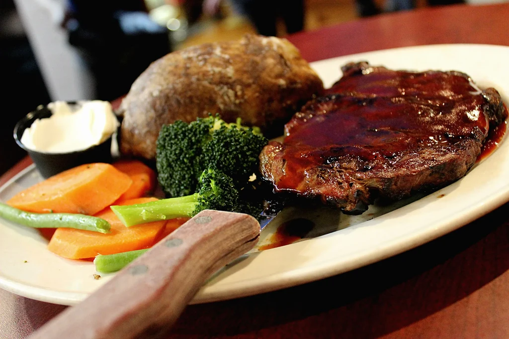 Plated meal of steak, baked potato, mixed vegetables, and a steak knife.