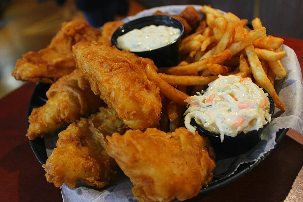 Close-up of battered fish and chips, tartar sauce, coleslaw in a basket.