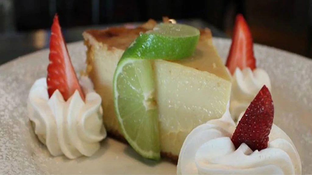 Light yellow cheesecake with lime, whipped cream, and strawberry wedges.
