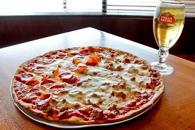 Pepperoni and sausage pizza with Stella Artois beer on a wooden table.