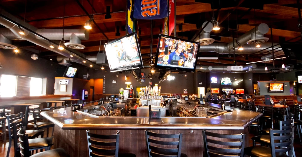 Modern sports bar interior with horseshoe bar, beer taps, TVs, and banners.