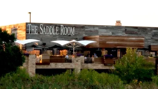 Exterior of The Saddle Room restaurant, modern wood building with patio dining.