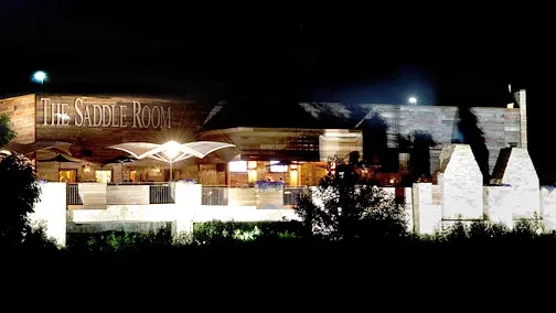 Exterior of "THE SADDLE ROOM" building at night with lit patio.