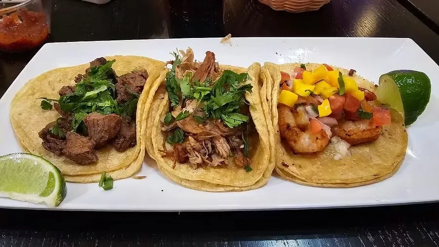 Plate of three tacos: steak, carnitas, and shrimp with salsa.