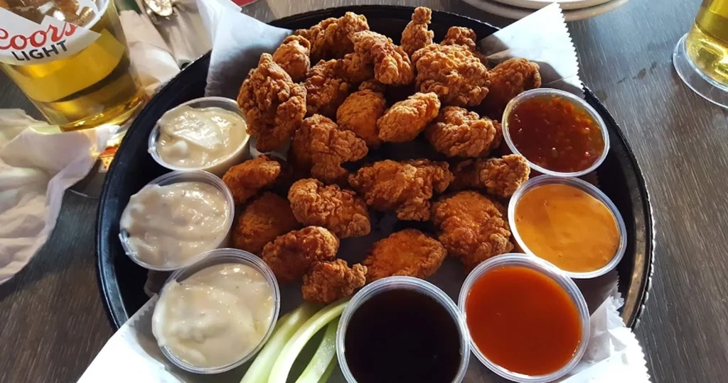 Close-up of fried chicken, various sauces, celery, and beer.