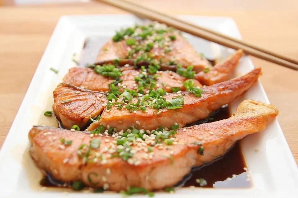 Pan-seared salmon with green onions, sesame seeds, and chopsticks on a white plate.