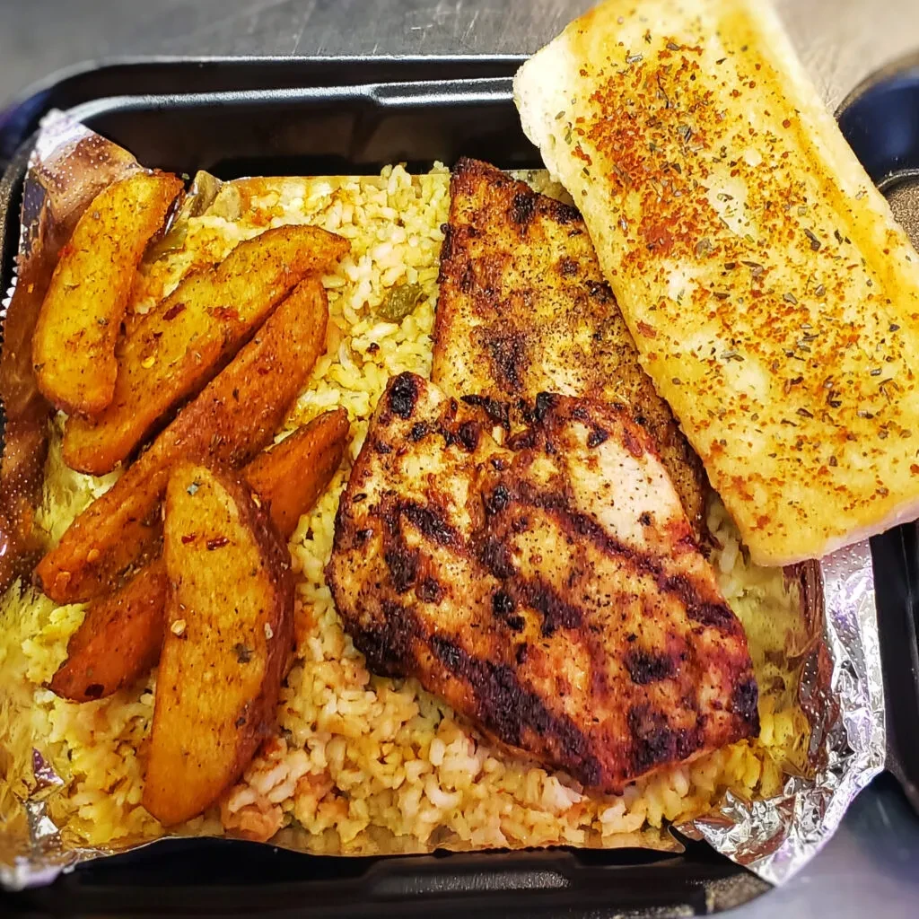 Grilled chicken, seasoned rice, potato wedges, and herb-topped bread.