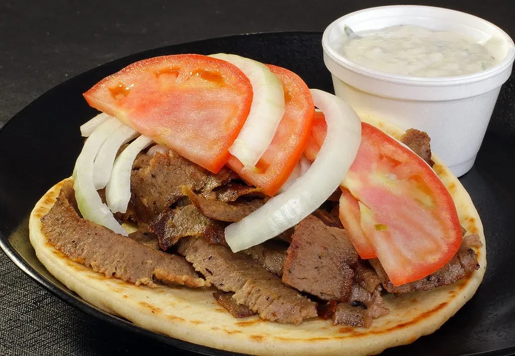 Gyro with thinly sliced meat, tomatoes, onions, and creamy sauce.