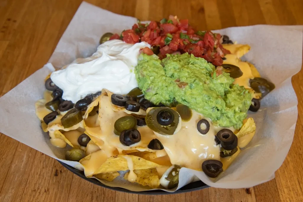 Close-up of nachos with cheese, guacamole, sour cream, tomatoes, olives, and jalapeños.