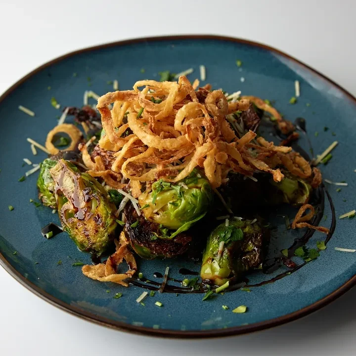 Roasted Brussels sprouts with fried onions, herbs, cheese, and glaze.