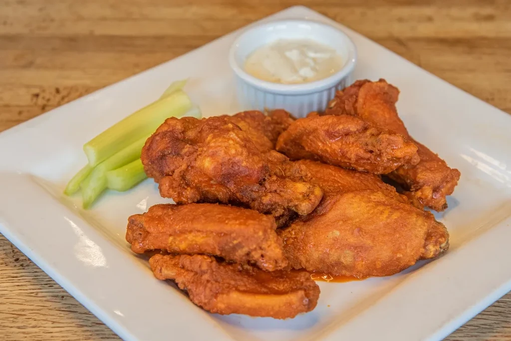 White plate of buffalo wings, celery, and dipping sauce.