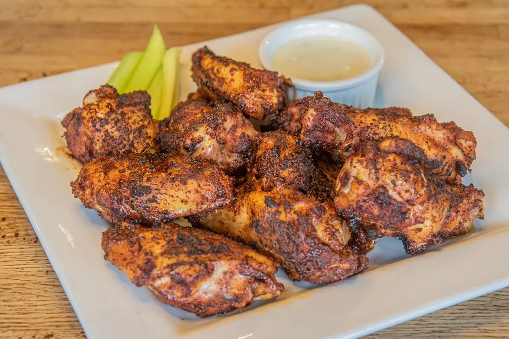 A plate of seasoned chicken wings with celery and dipping sauce.