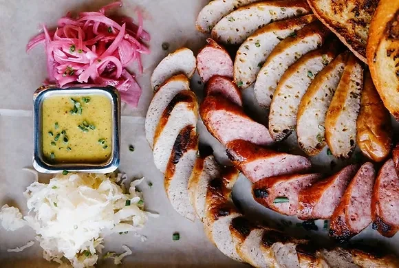 Platter of sliced sausages with pickled onions, mustard, sauerkraut, and bread.