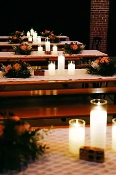 Rustic wooden tables with candles and orange rose floral arrangements.