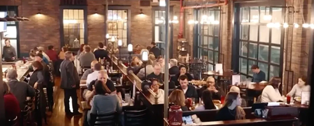 Bustling restaurant interior with patrons, brick walls, and warm lighting.