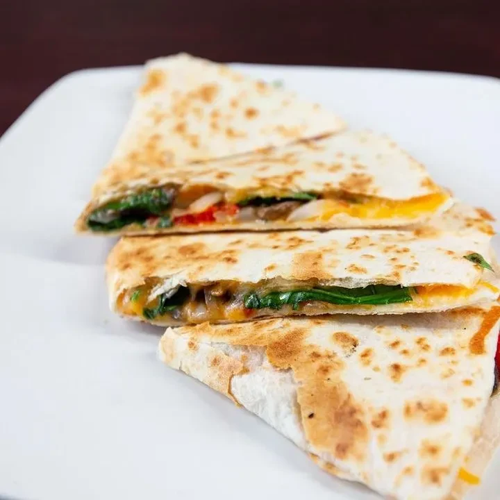 Quesadilla pieces with melted cheese, spinach, mushrooms, and red vegetables.