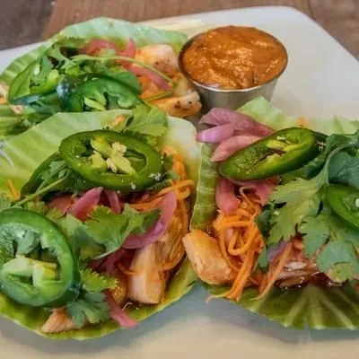 Lettuce wraps with meat, vegetables, cilantro, jalapeños, and sauce.