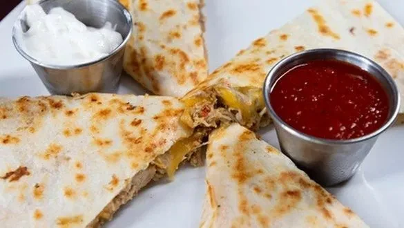 Plate of golden-brown quesadilla triangles with meat, sour cream, and red sauce.