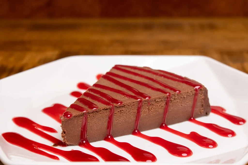 Chocolate cheesecake slice with red berry sauce on a white plate.