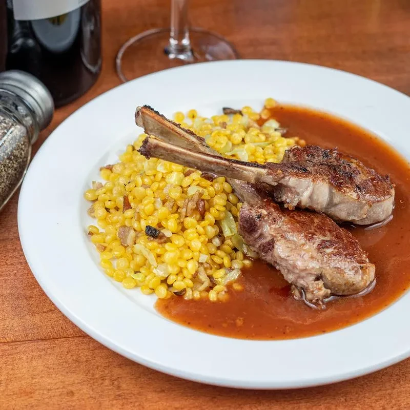 Two grilled lamb chops, pearl-shaped grains, and sauce on a plate.