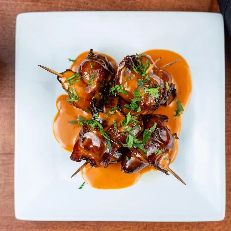 Four skewered food items coated in glossy sauce on a white plate.