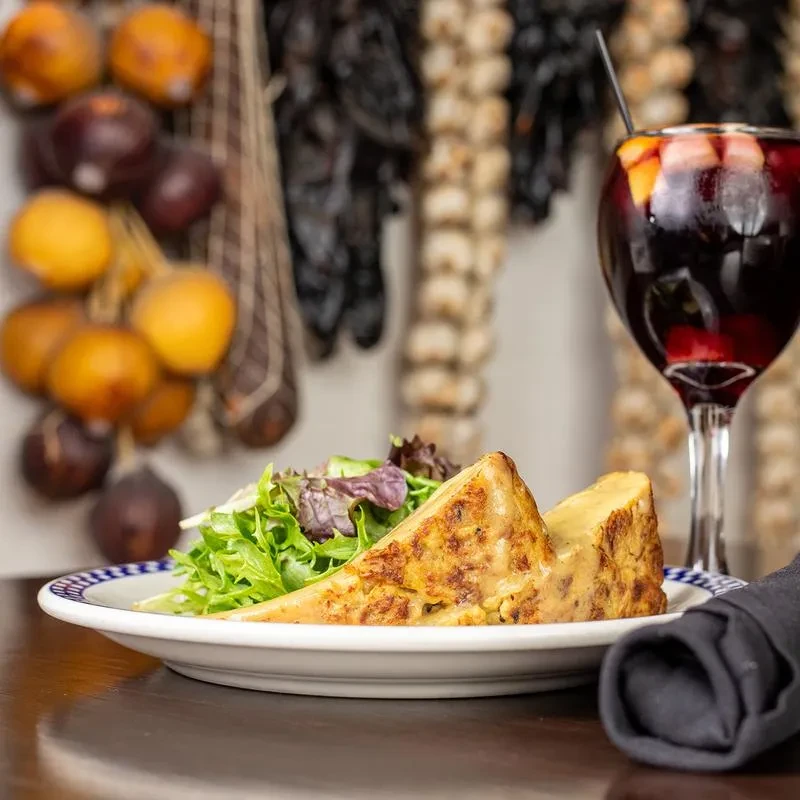 A slice of Spanish tortilla, salad, and sangria on a white plate.