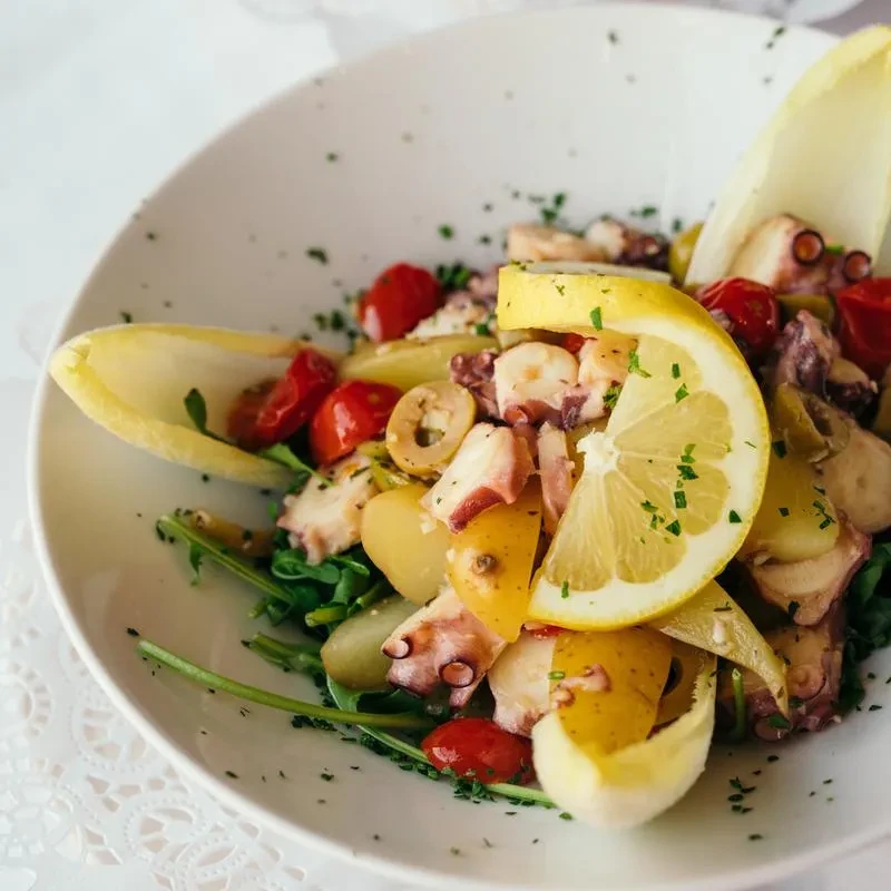 Close-up of an octopus salad with tomatoes, olives, potatoes, and greens.
