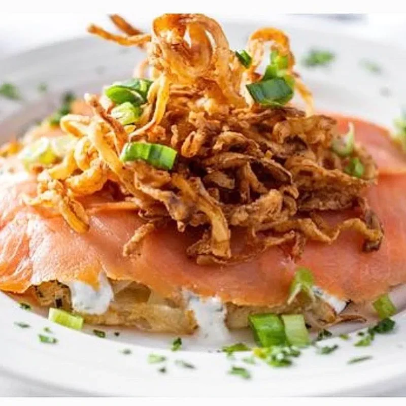 Smoked salmon appetizer with dill sauce, fried onions, and chives.
