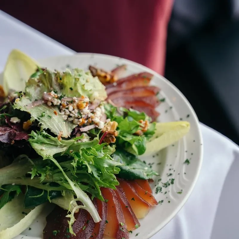 A close-up shot of a salad with greens, cheese, nuts, and meat.
