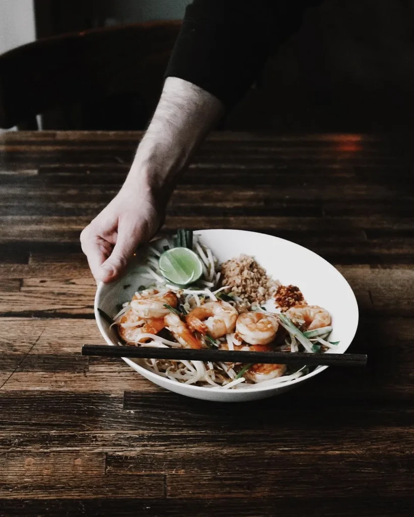Pad Thai with shrimp, lime, and peanuts on a wooden table.