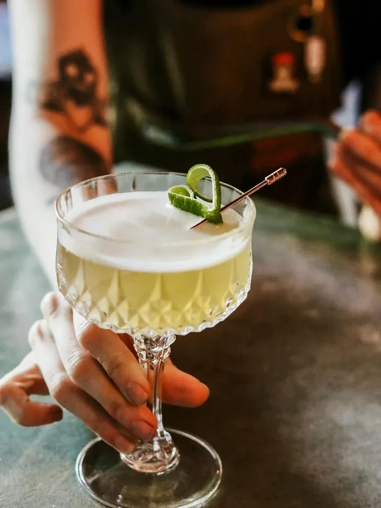 Close-up of a frothy yellow cocktail in an ornate glass.