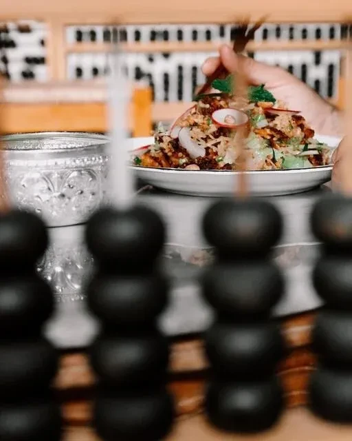 Hand holding tongs, tossing a salad bowl on a white plate.