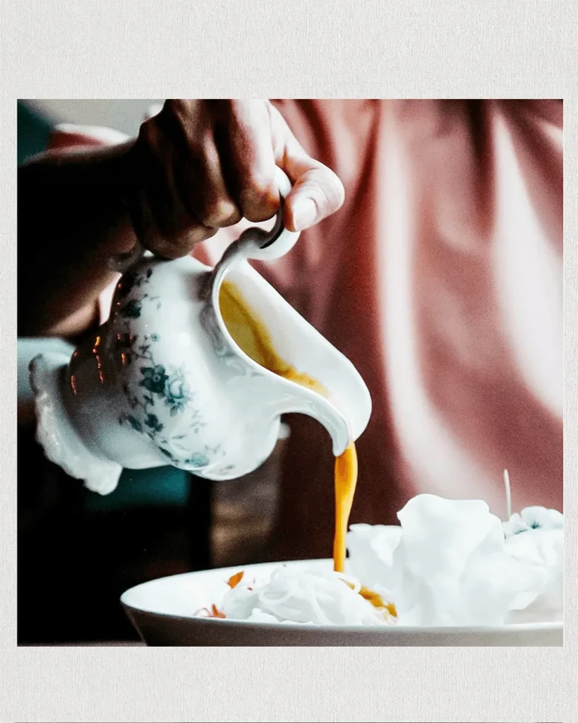 Hand pours golden liquid from a floral pitcher into a white bowl.