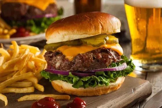 Gourmet cheeseburger, French fries, and beer on a wooden board.