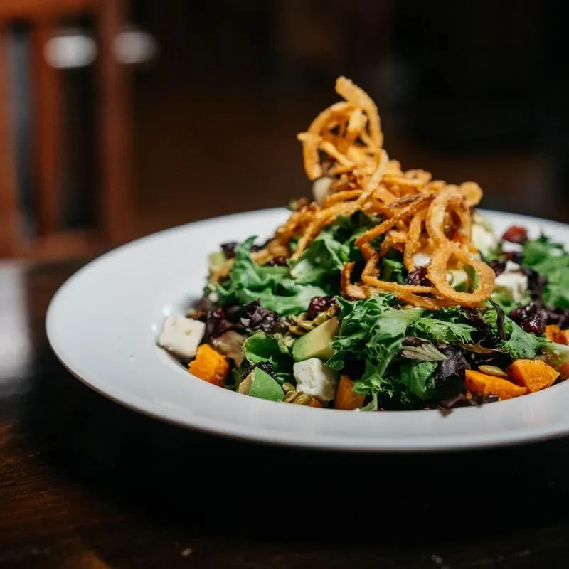Close-up of a salad with greens, avocado, feta, sweet potato, and fried onions.
