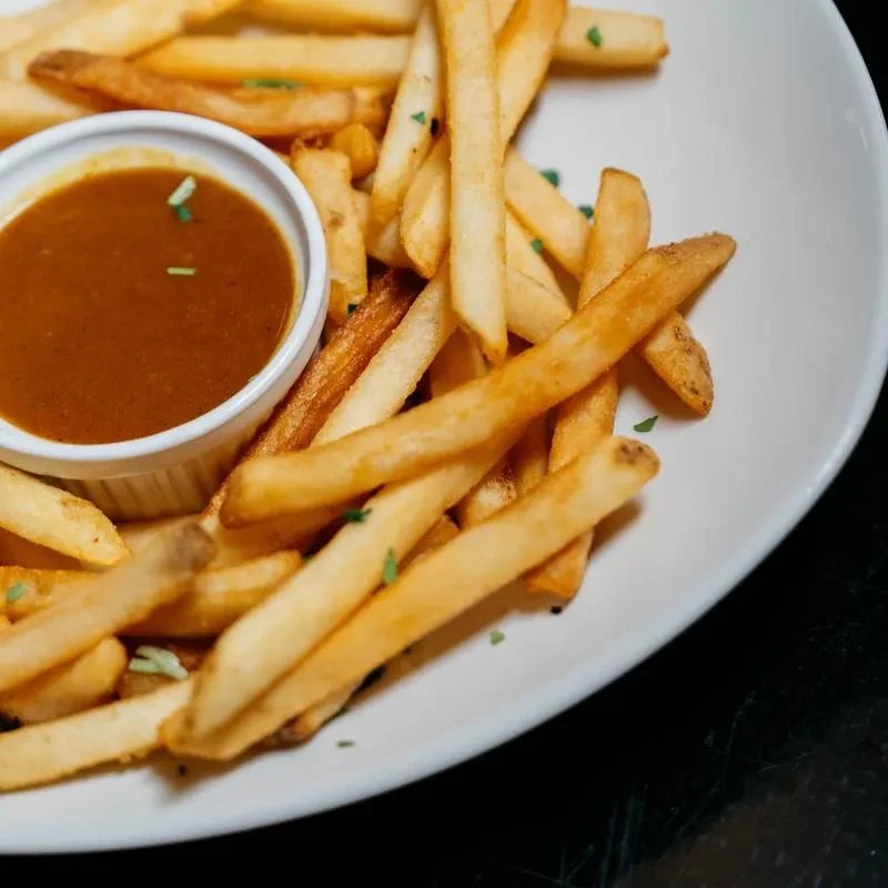Plate of golden-brown french fries with a side of dark dipping sauce.