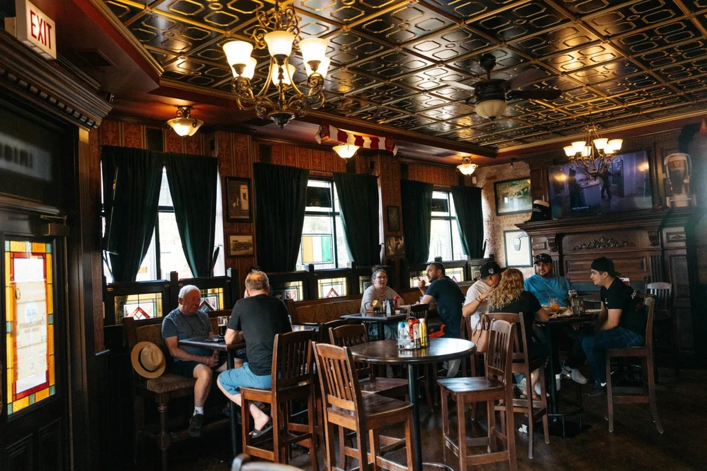 Dimly lit restaurant interior with patrons, wood paneling, and chandeliers.
