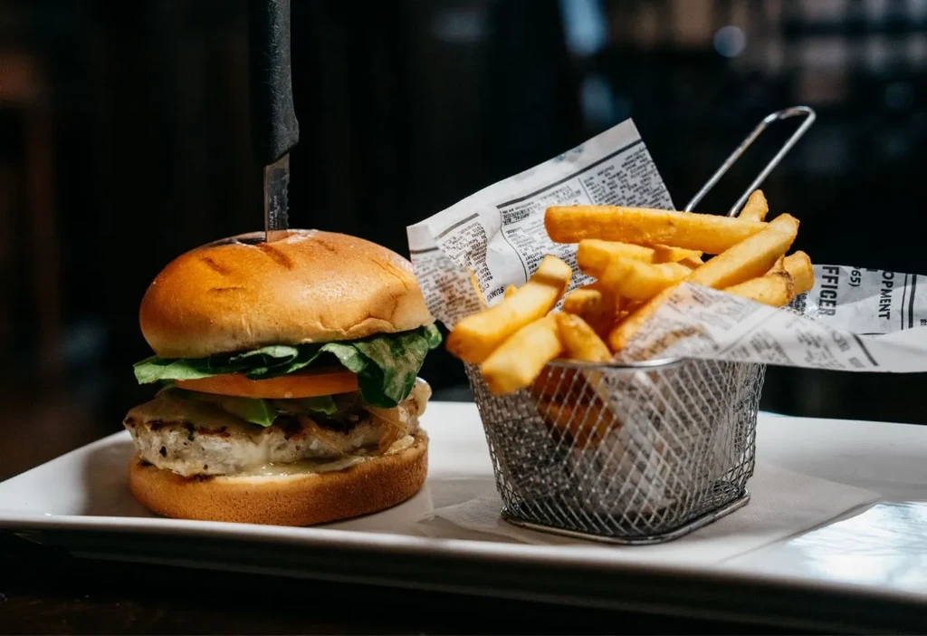 Gourmet burger with knife, fries in basket on white plate.