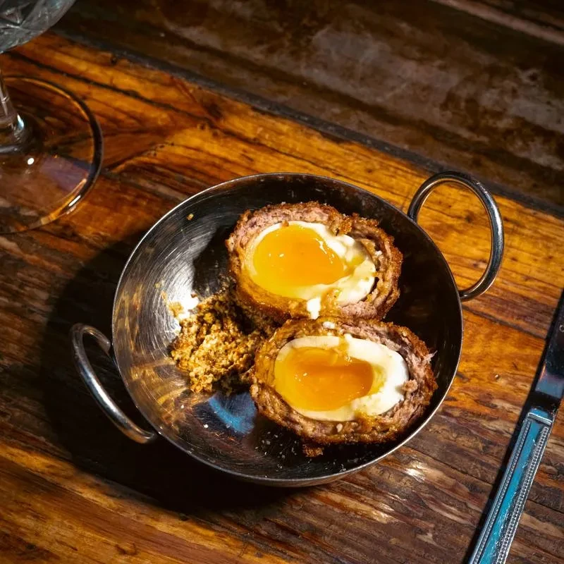 Two halved Scotch eggs with runny yolks in a metal bowl.