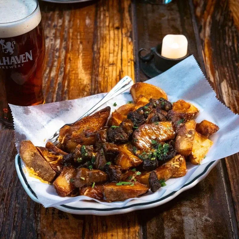 Plate of roasted potatoes, meat, gravy, and herbs with a beer.
