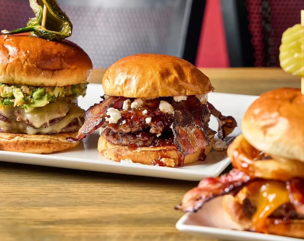 Three gourmet burgers with diverse toppings on white plates.
