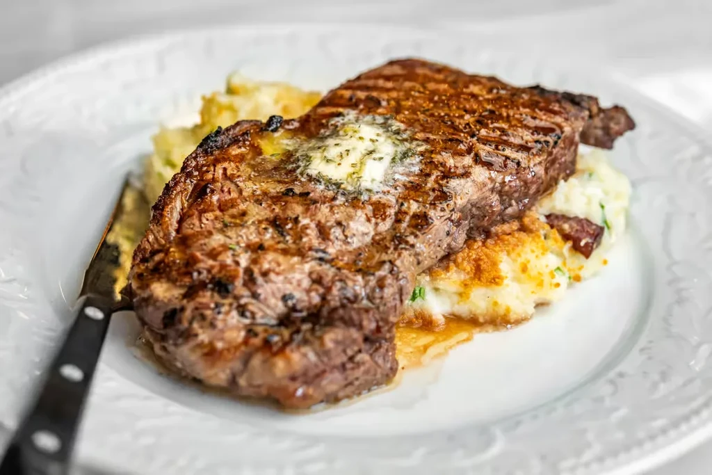 Close-up of a perfectly cooked steak with butter on mashed potatoes.