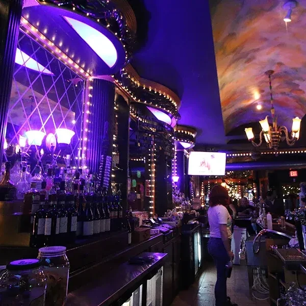 Dimly lit bar with purple lights, reflective mirrored wall, and bottles.
