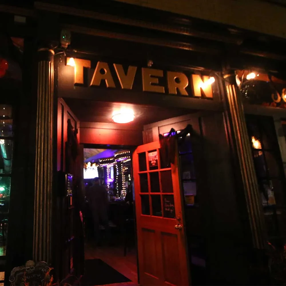 Illuminated "TAVERN" sign above a doorway with fluted columns.