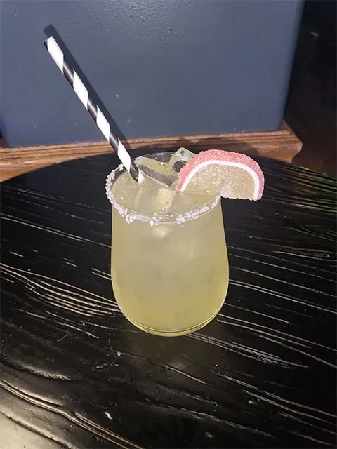 Salt-rimmed cocktail with lime and striped straw on a dark table.