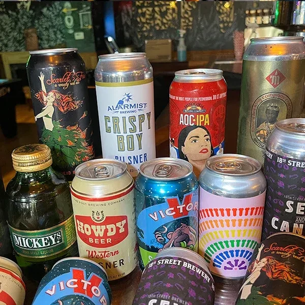 Assorted beer cans and one malt liquor bottle on a wooden table.