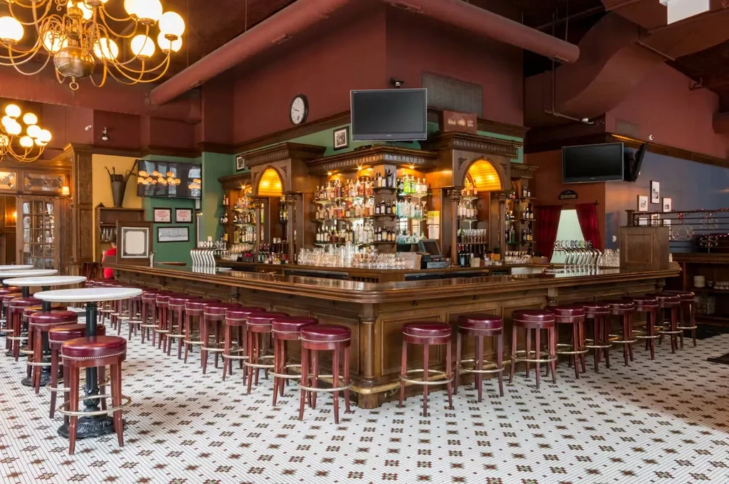 Ornate U-shaped bar with red stools, mosaic floor, and chandeliers.