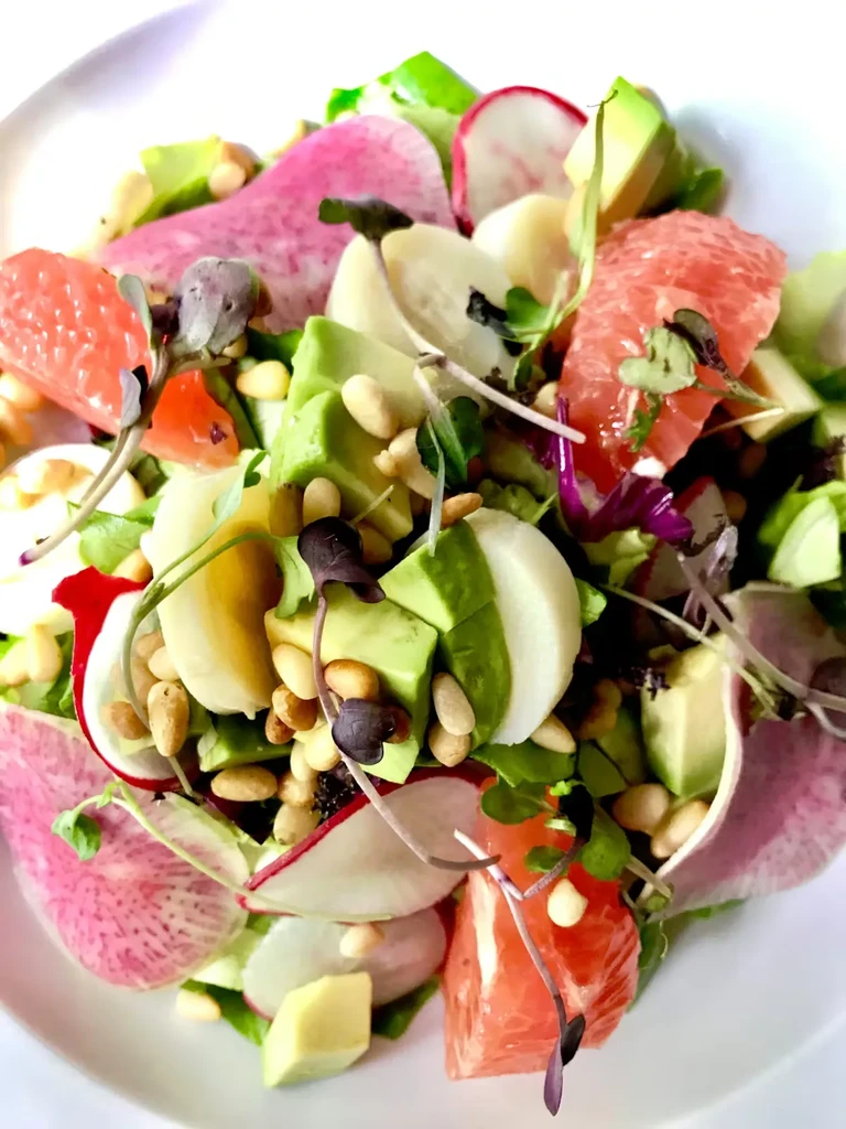 Overhead shot of a salad with grapefruit, avocado, radishes, and greens.