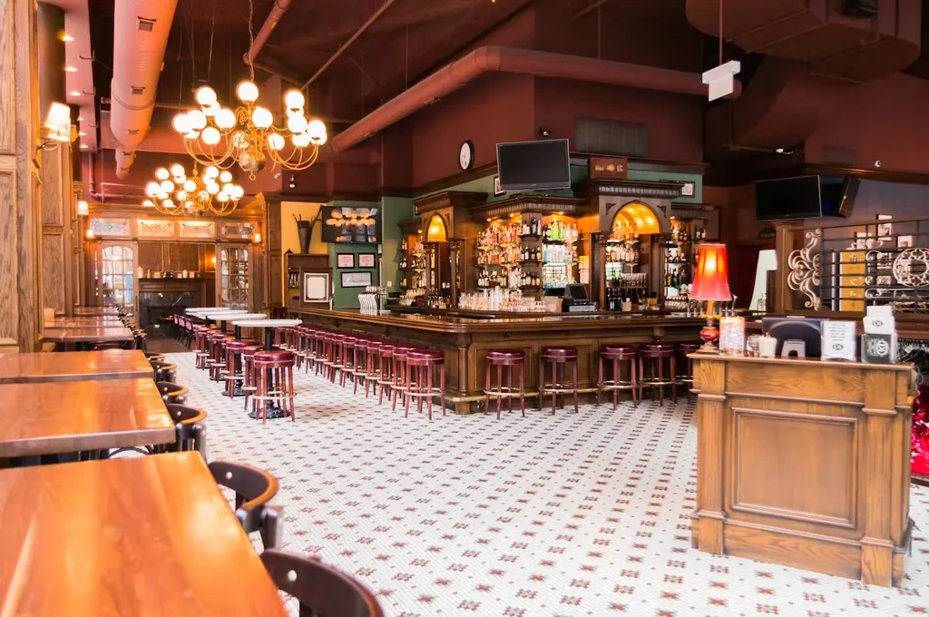 An empty bar with a wooden L-shaped counter and red barstools.